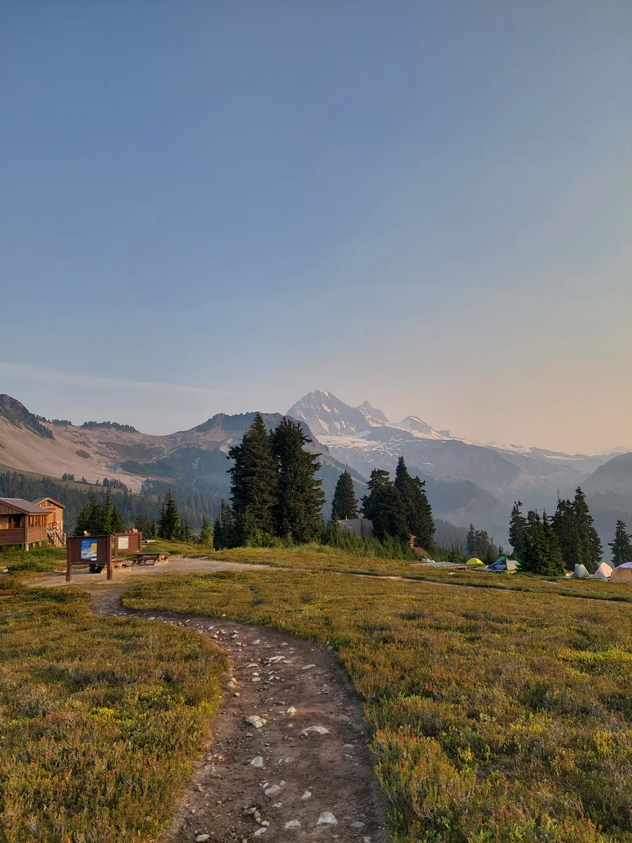 A rocky footpath across a meadow toward sunlit mountains