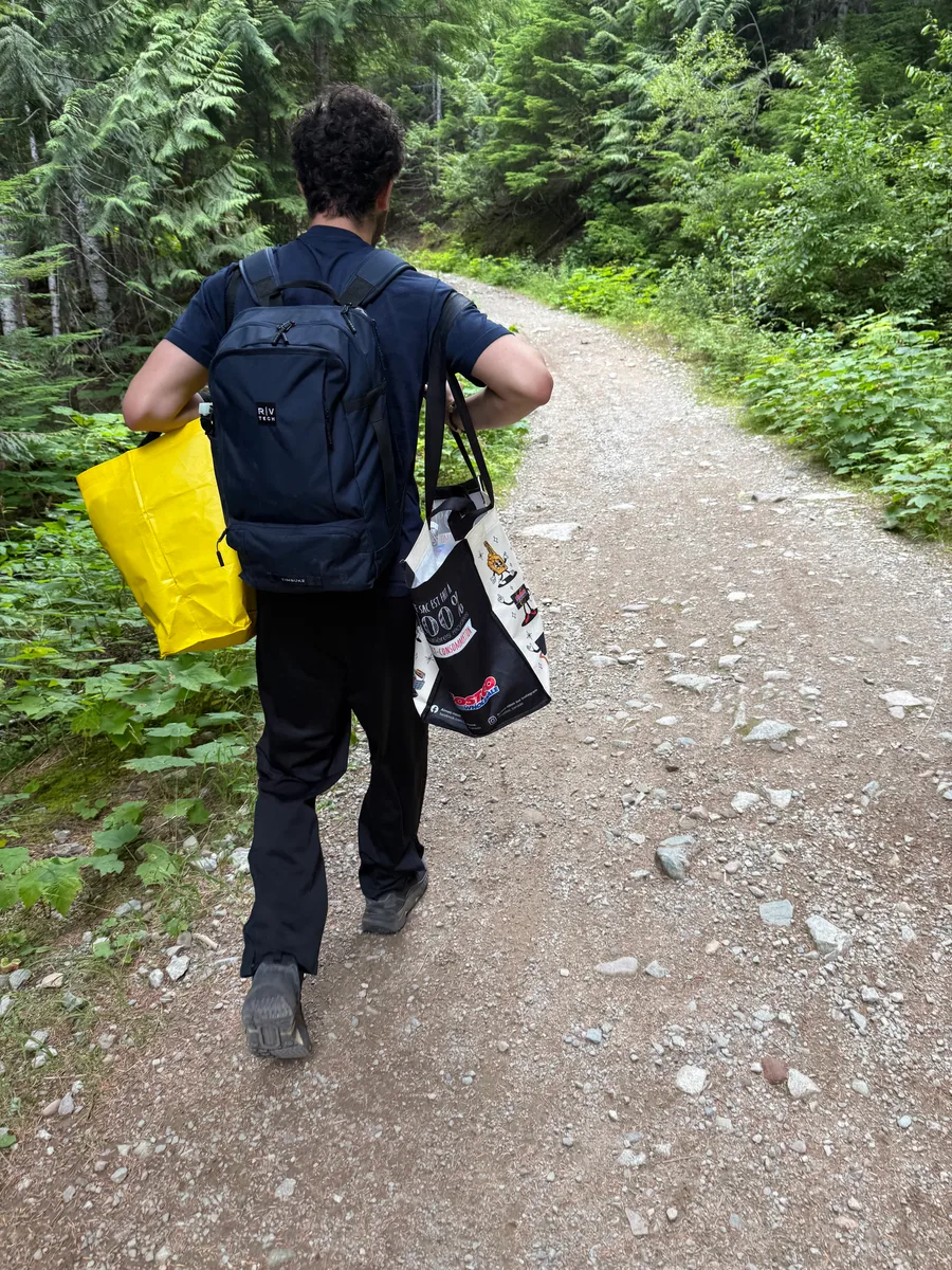 A hiker carrying a backpack and bags along a forest trail