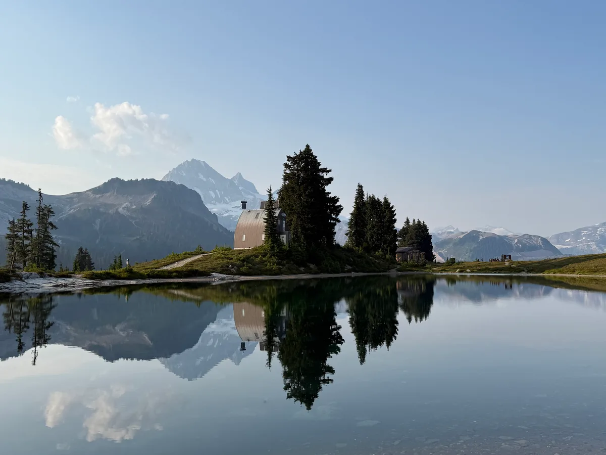 Evergreen trees and a lakeside cabin reflected in calm water