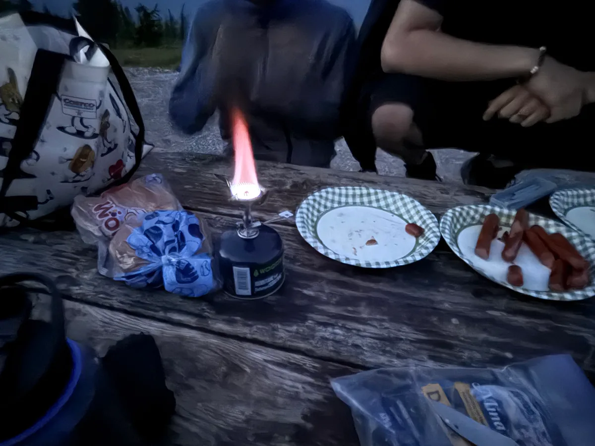 A glowing camping light and plates of food on a picnic table at dusk