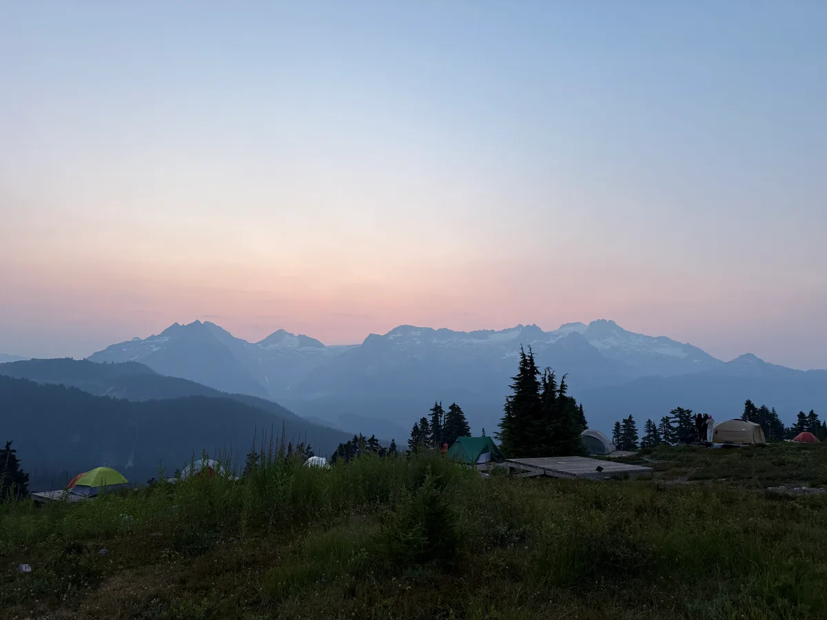 Tents and wooden camping platforms overlooking mountains at dawn