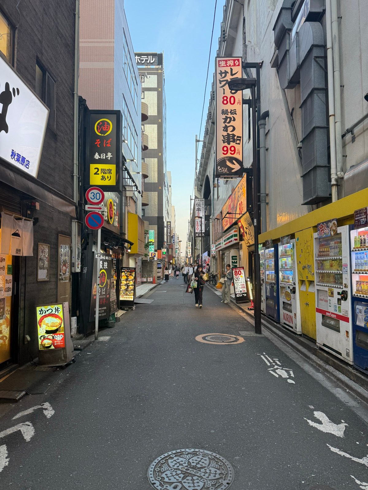 A narrow shopping street lined with restaurant signs and vending machines