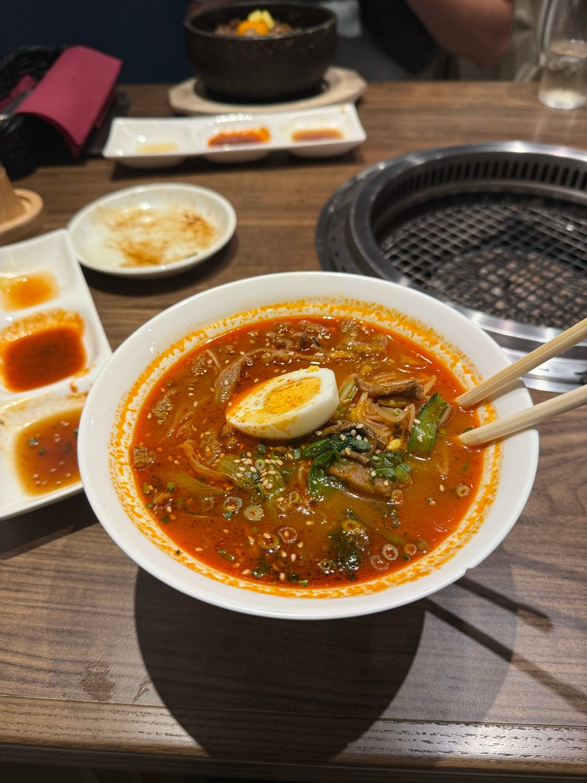 A bowl of red soup topped with half an egg beside a tabletop grill