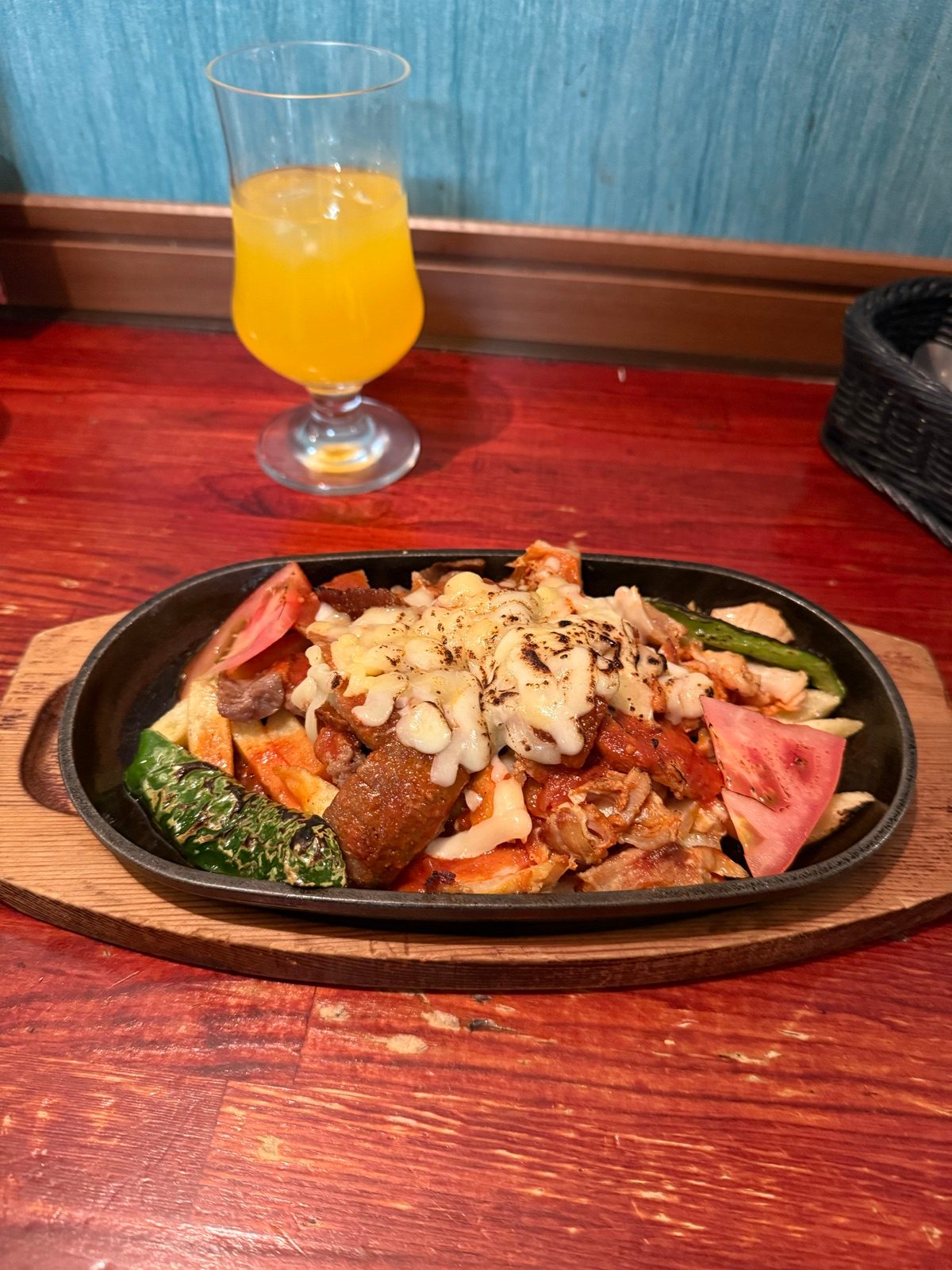 A sizzling platter of meat and vegetables with an orange drink