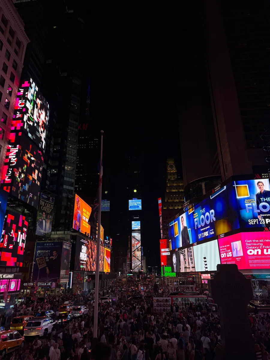 Crowds beneath brightly lit Times Square billboards at night