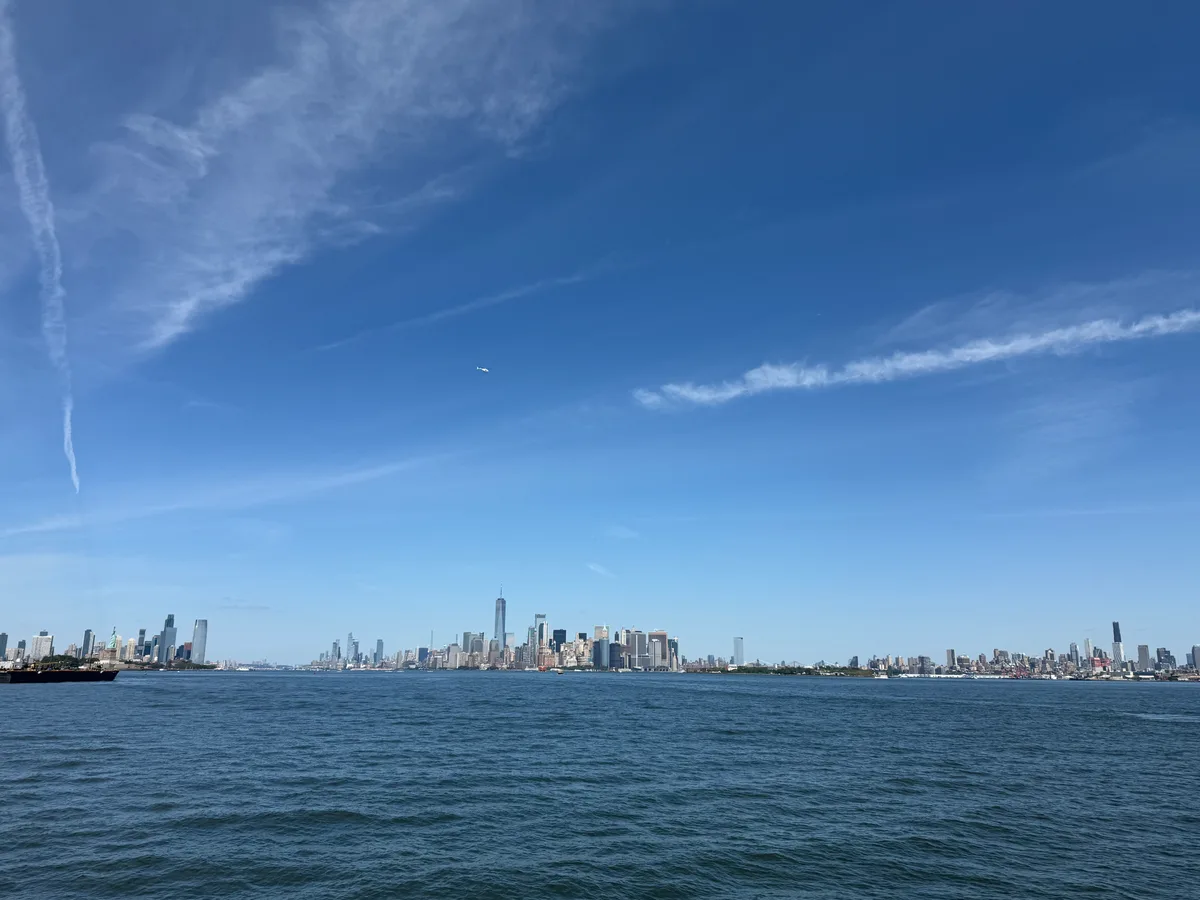 The Manhattan skyline across the harbor beneath a blue sky