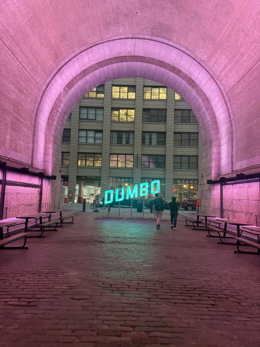 A glowing DUMBO sign beneath a pink-lit brick archway