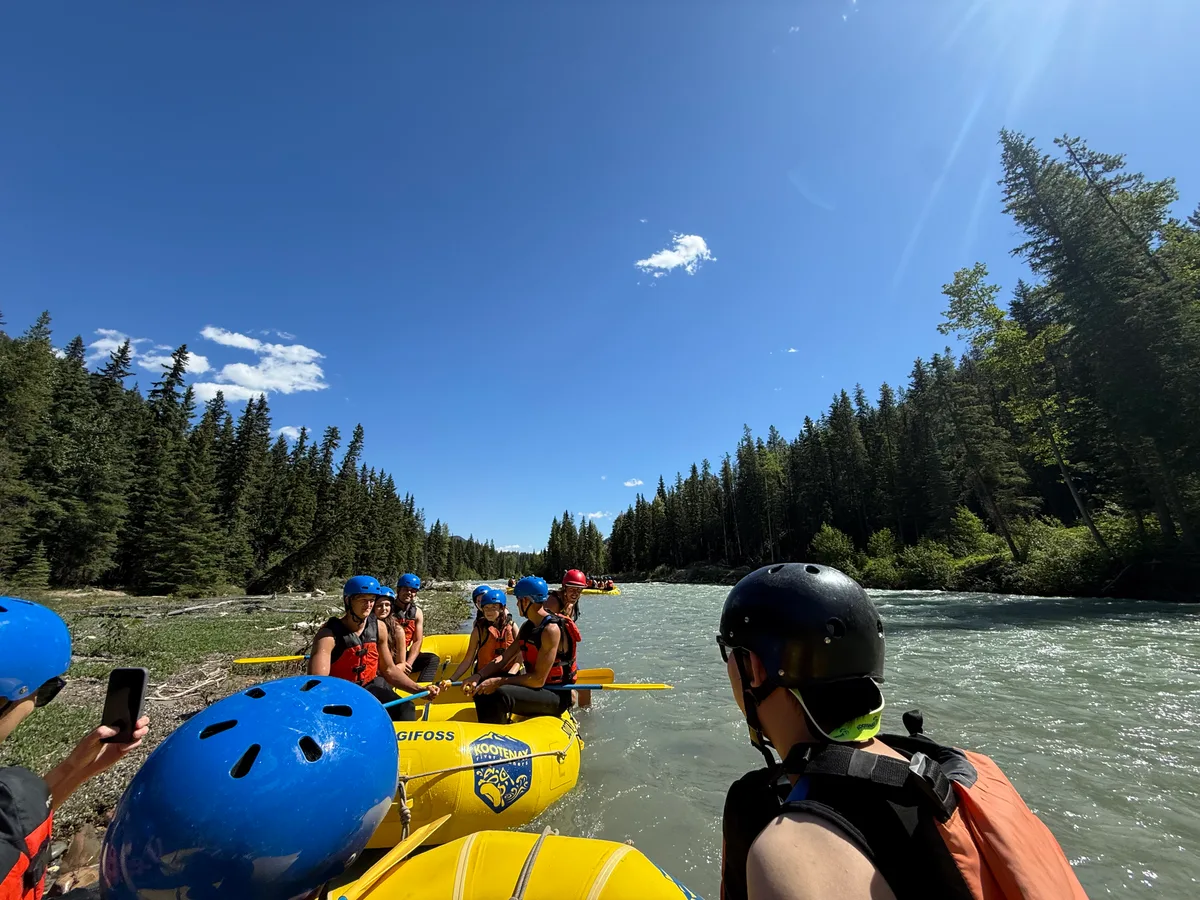 Rafters in helmets and life jackets on a river bordered by evergreen forest