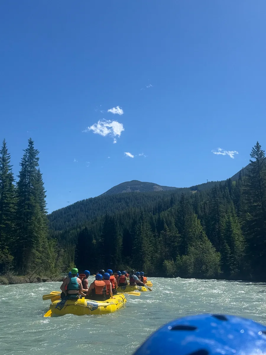 A yellow raft approaching rapids beneath a forested mountain