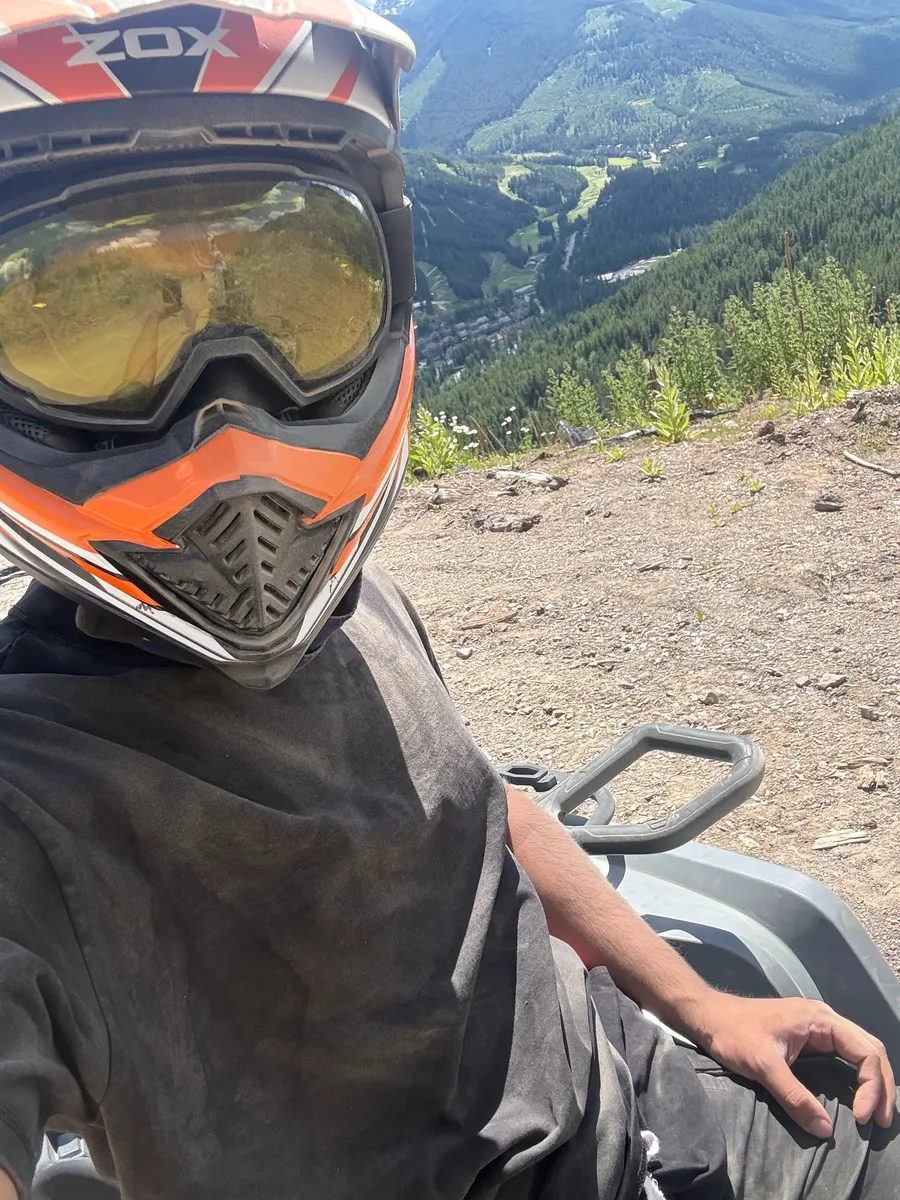 A helmeted rider on an ATV overlooking a green mountain valley