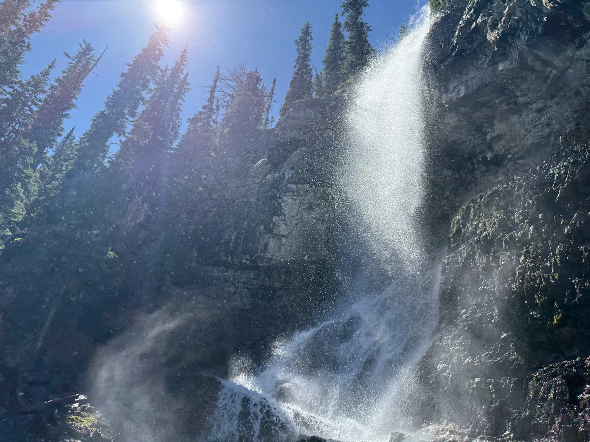 Spray from a tall waterfall catching sunlight beside a rock face