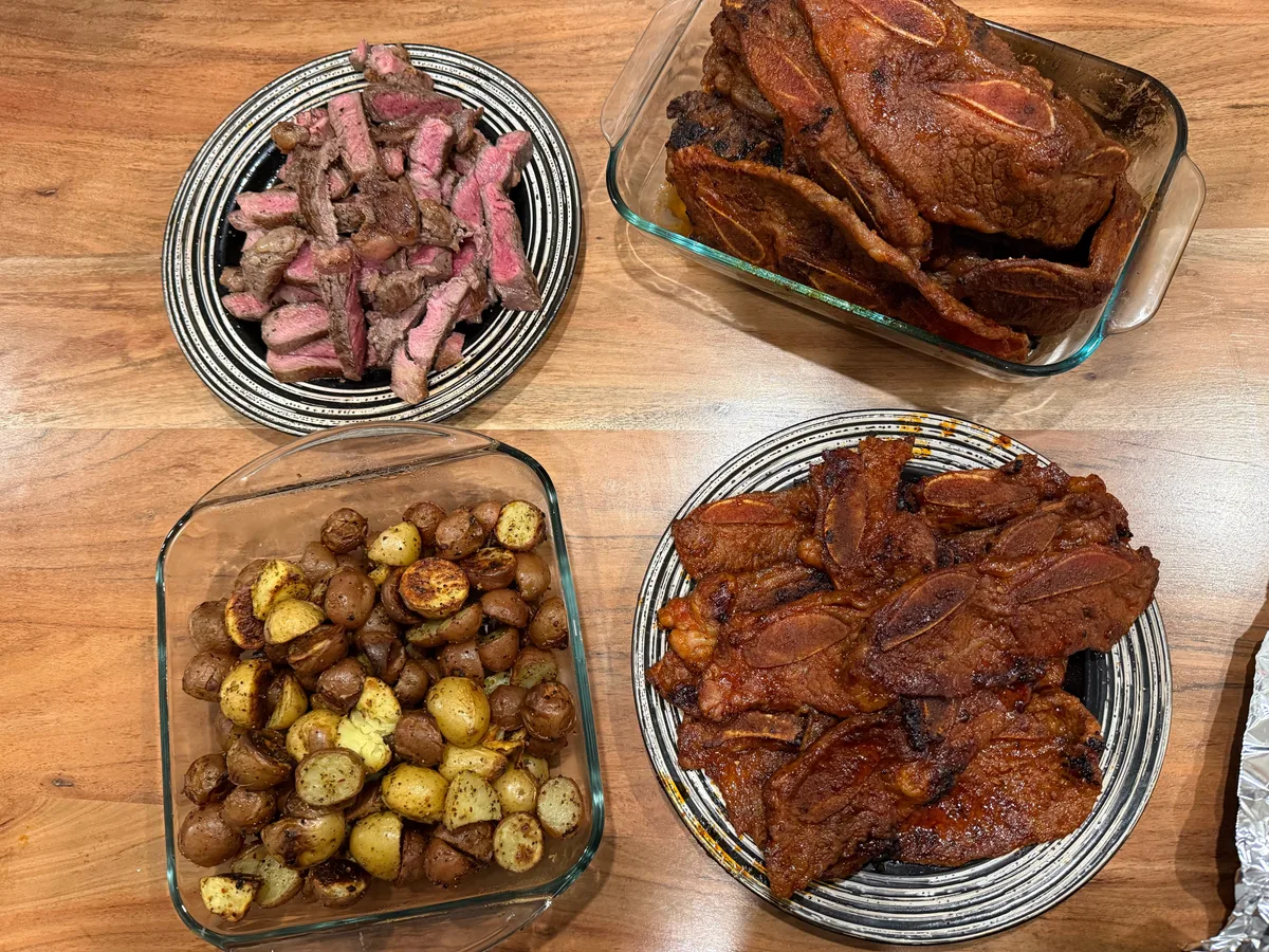 Platters of cooked meat, roasted poultry, and potatoes on a table
